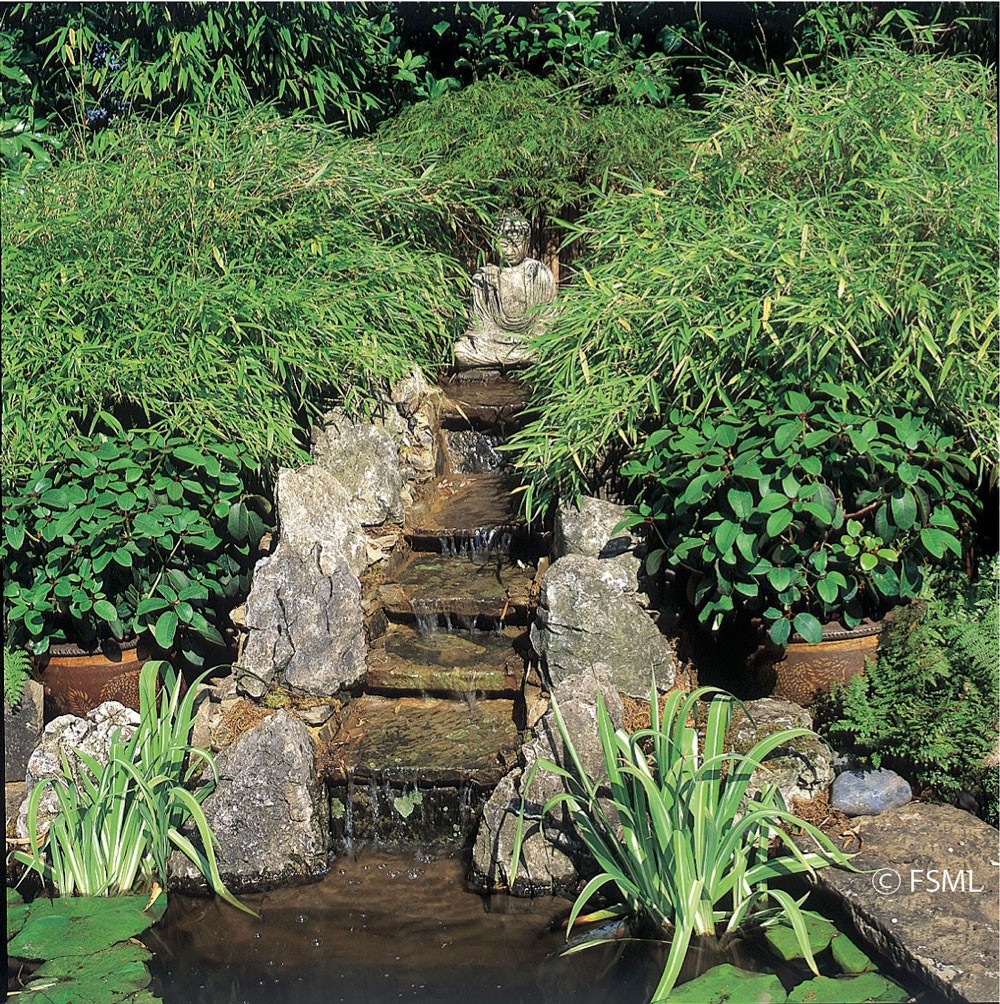 Stone buddha presides over a water cascade edged with bamboo.
